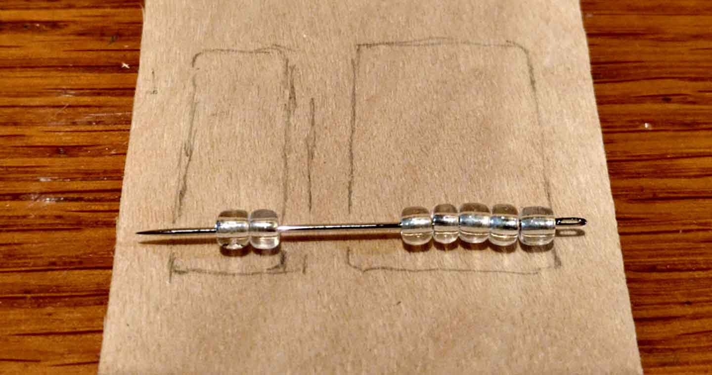 sewing pins and clear beads laid out for size of the abacus on a sheet of veneer